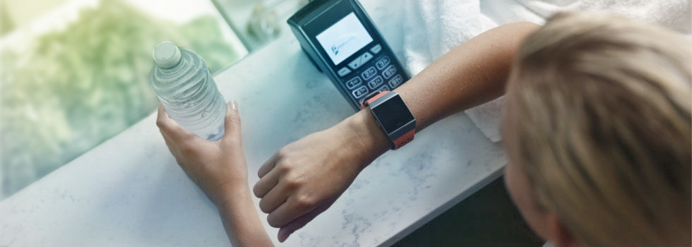 Eine junge Frau bezahlt ihr Getränk mit ihrer Garmin Smartwatch.